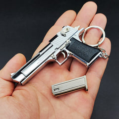 Metallic gun-shaped keychain held in a hand against a dark background