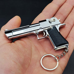 Hand holding a silver gun-shaped keychain with a black grip on a dark background