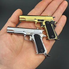 Two miniature gun keychains, one gold and one silver, held in a hand against a dark background.