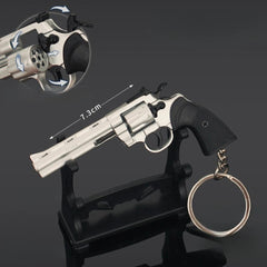 Revolver model on a stand with measurement details and a keychain attached, on a dark background.