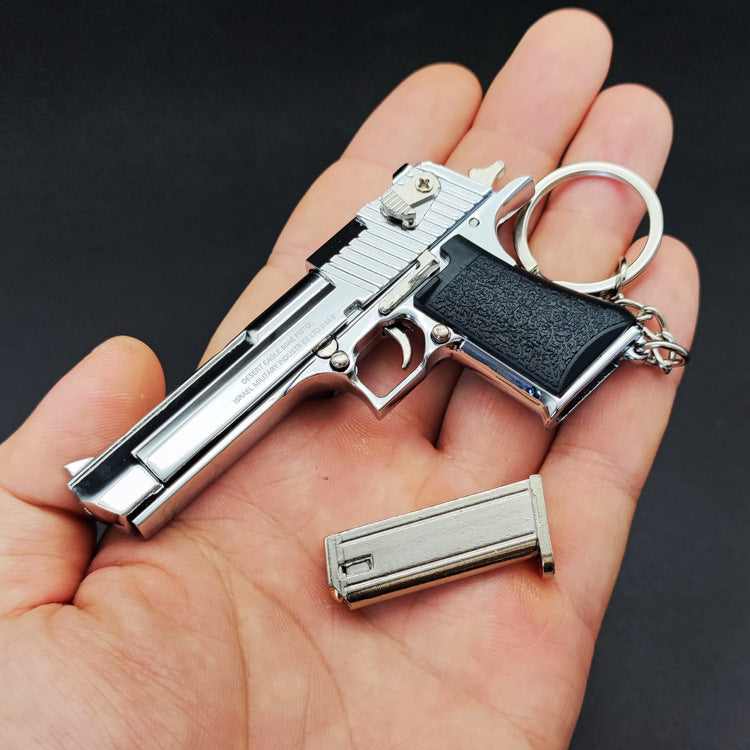 Metallic gun-shaped keychain held in a hand against a dark background