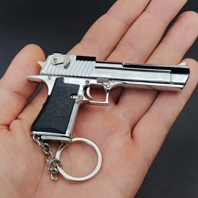 Hand holding a silver gun-shaped keychain with a black grip on a dark background