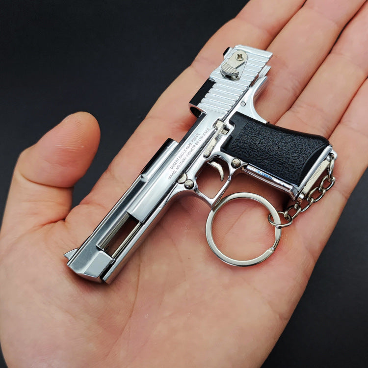 Metallic gun-shaped keychain held in a hand against a dark background