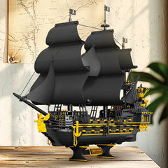 Model of a pirate ship with black sails and yellow details on a wooden platform.