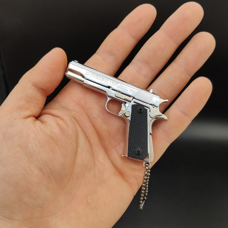 Small silver gun-shaped object held in a hand against a black background