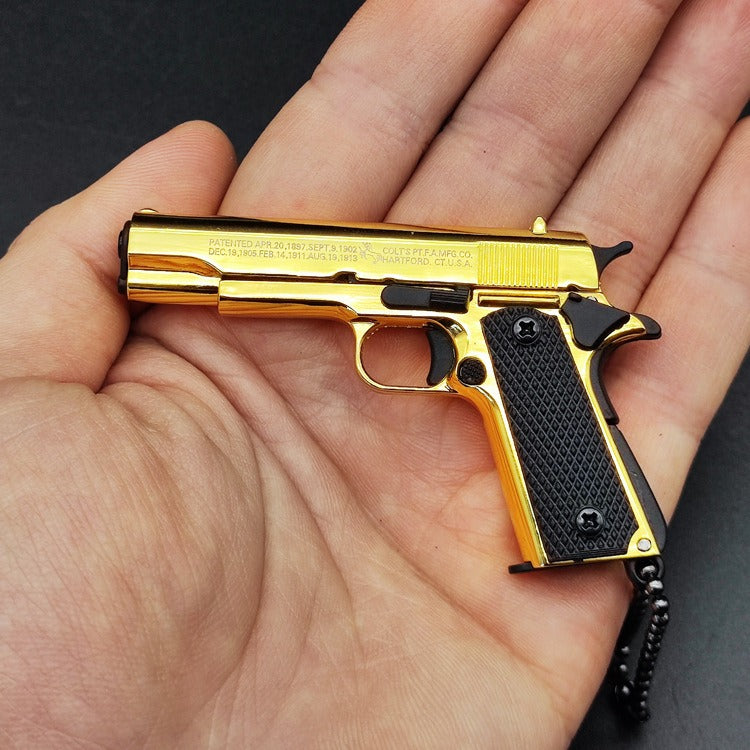 Gold and black gun-shaped keychain held in a hand against a dark background