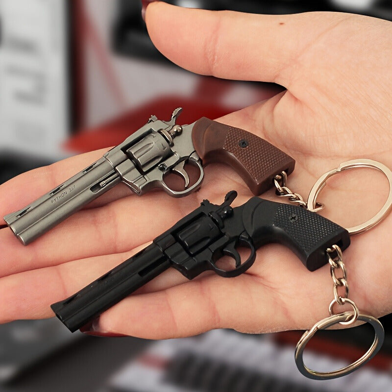 Two miniature revolver keychains held in a hand with a blurred background.