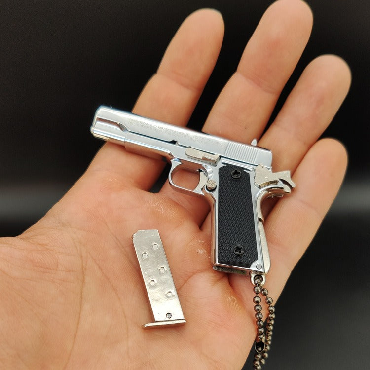 Metallic gun-shaped keychain with a magazine on a hand against a dark background