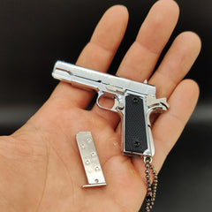Metallic gun-shaped keychain with a magazine on a hand against a dark background