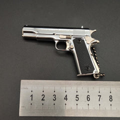 Metallic gun-shaped keychain with black grip on a gray background, accompanied by a ruler for scale.